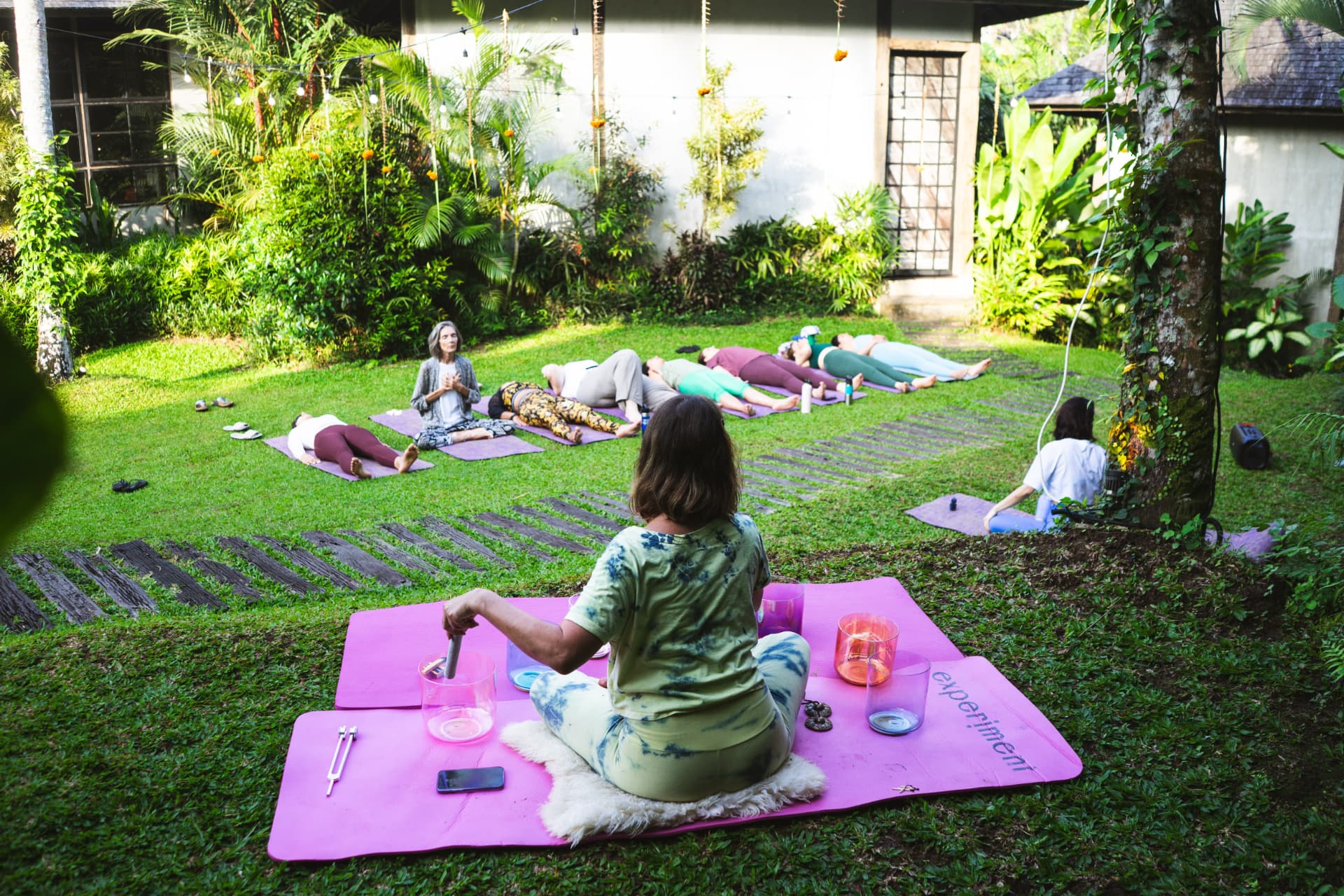 Outdoor sound healing session on the grass with participants resting on mats.
