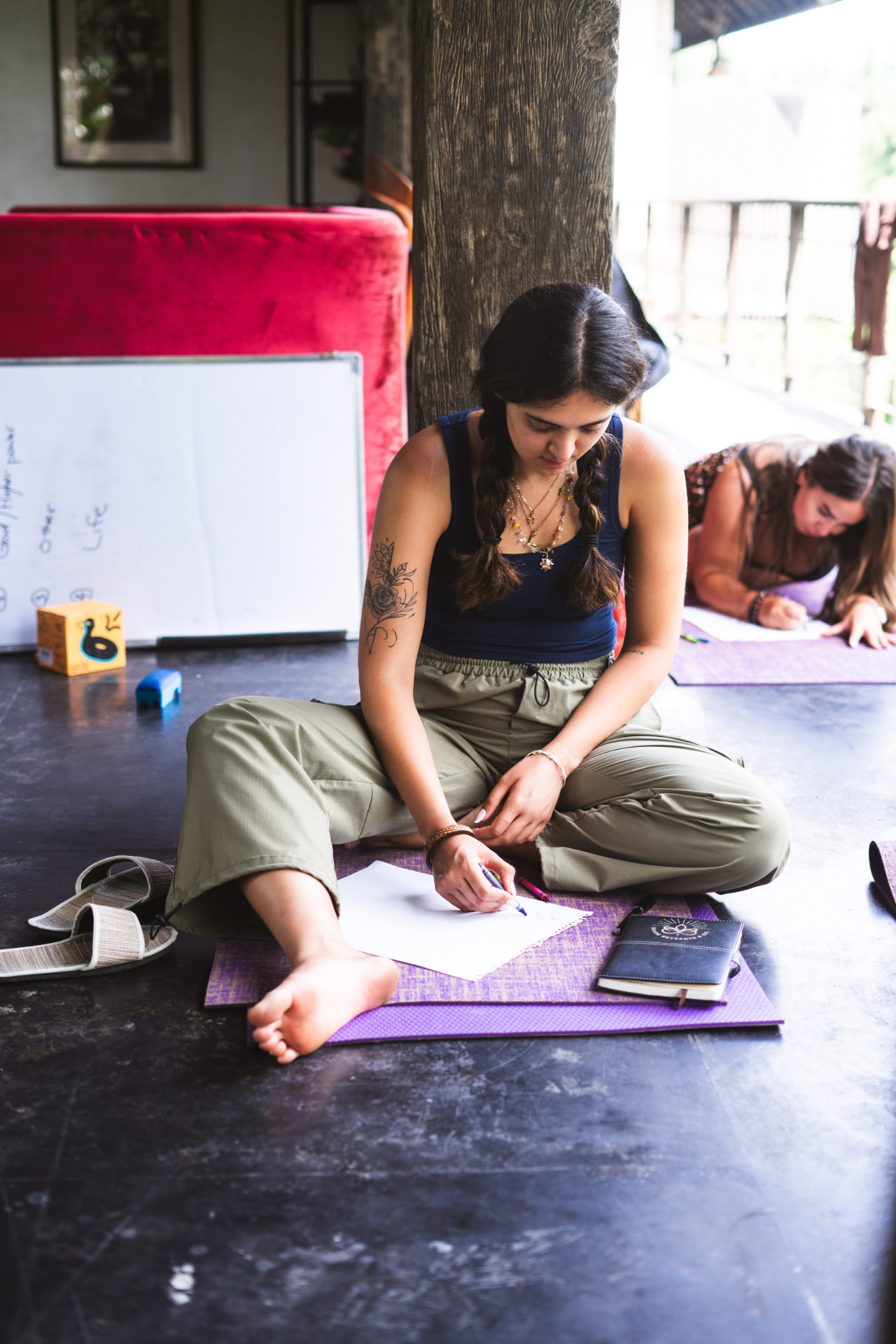 Participant drawing on paper while seated cross-legged on a yoga mat.